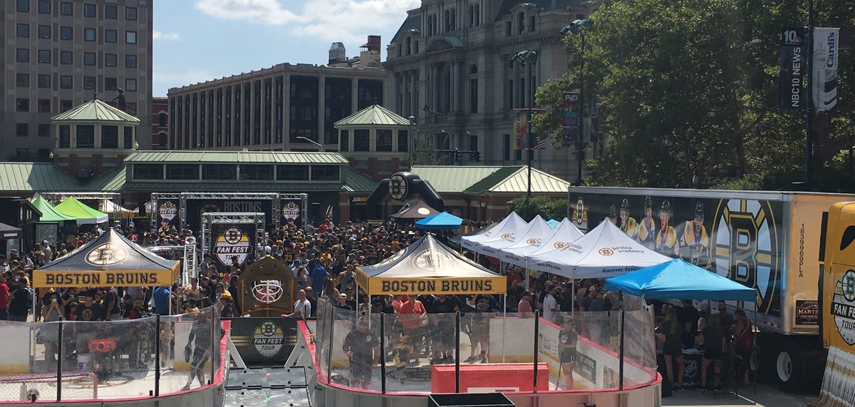 Wide view of the Boston Bruins Fan Fest Tour footprint in a downtown plaza, with a synthetic-ice rink and branded tents